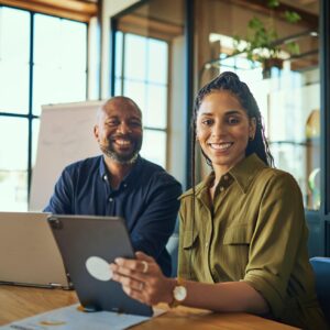 Cheerful female executive and colleague smiling at camera in boardroom